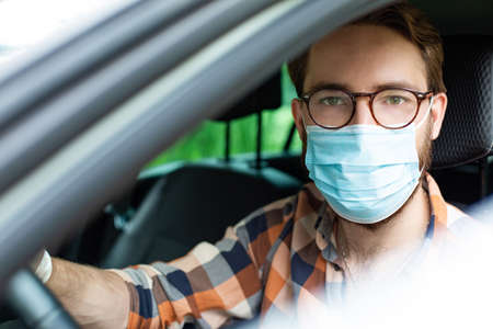 Male driver with protective gloves and a face mask, sitting in a car. Everyday prevention against infections and viruses.の写真素材