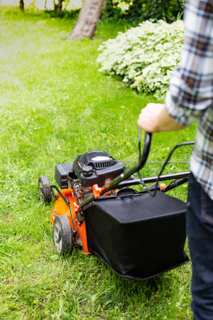 Gardening. Greenworks. Man mowing grass using a petrol lawnmower with a high-capacity grass box....