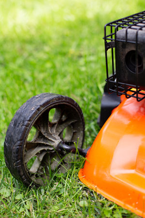 Gardening. Greenworks. Mowing a lush, leafy green lawn by petrol mower, gasoline lawnmower in a garden on a sunny day. Close-up on a lawnmower wheel.の写真素材