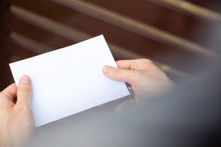 Male hands holding a letter, close up, focus on letter. Sending, receiving, reading mail, message. Traditional mail, correspondence. Envelope with a copy-space. Postman. Checking a letterbox.の写真素材