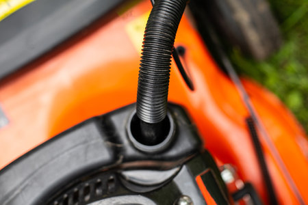Refilling a fuel tank in a petrol lawn mower with a canister with a funnel, close up on a funnel. Gardening, greenworks, using a gasoline lawn mower in a garden on a sunny dayの写真素材