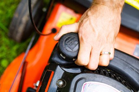 Refilling, opening a fuel tank in a petrol lawn mower, close up on a hand on fuel filler cap. Male...