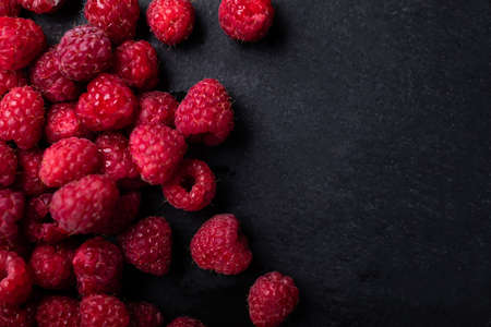 Fresh, ripe, appetizing raspberries scattered on a black, stony background, top view with a text space, a copy-space. Berries, seasonal fruits.の写真素材