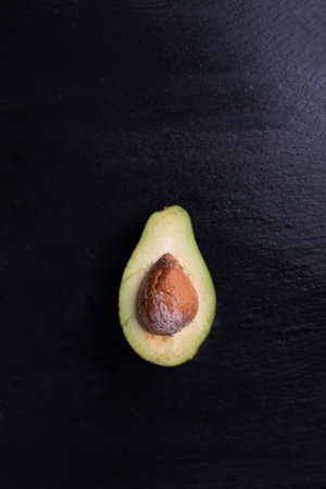 Halved, ripe avocado with a pit, seed, on a black, stony background, top view with a copy-space, text space. Vegan, raw delicacy. Tasty healthy veggies. A dieting concept, food minimalist composition.の写真素材
