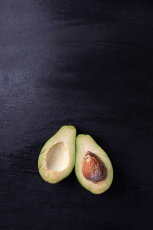Vertical view of a ripe, halved avocado with a pit on black, stony background, top view with a copy-space, text space. Vegan, raw delicacy. A tasty healthy veggies. A dieting concept, food compositionの写真素材