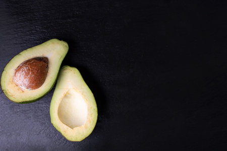 Horizontal view of a ripe, halved avocado with a pit on black, stony background, top view with a...