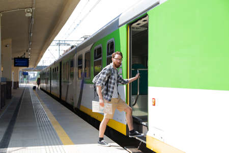 Tourist, traveller with a map, getting on a train on a platform on a suburban railway station.の写真素材