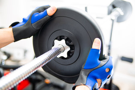 Male hands loading weight plates on a barbell, focus on a plate. Heavy weight exercise.の写真素材