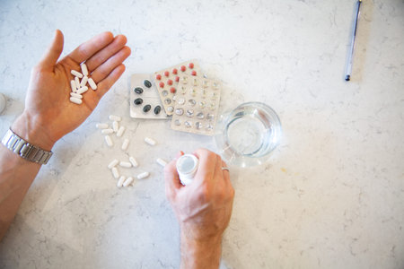 Top view on blisters of pills, scattered pills, glass of water and male hands holding a lot of pills...