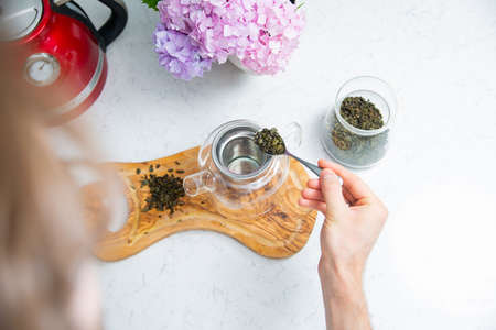 Making a perfect loose tea. Putting tea leaves by a teaspoon into a tea infuser in a glass teapot, top view.の写真素材