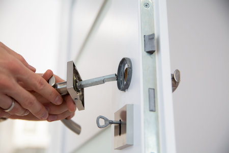 A broken metal handle in a wooden door during repairing by a handyman, close up. Small repairs of a...
