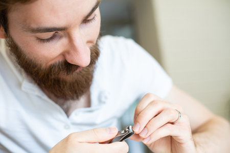 Young bearded man cuts his fingernails using a clipper, a nail cutter.の写真素材