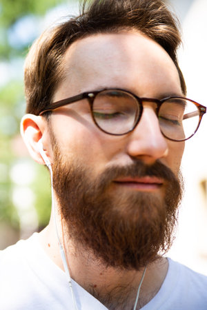 Young man with closed eyes listening to the music on a earphones, outdoor, close-up.