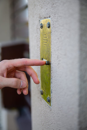 A male hand pressing a button on an outdoor doorbell with an intercom