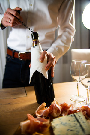 Wine tasting. A sommelier, a man in a white shirt uncorking a bottle of red wine with a corkscrew, a wine opener. Celebrating special occasion and drinking wine with family, friends.の写真素材