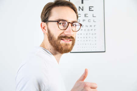 A young adult man smiling and looking at the camera after reading an eye test chart, a vision test board on a white wall. An ophthalmologist, an optometrist eye examination, a test for visual acuity.の写真素材