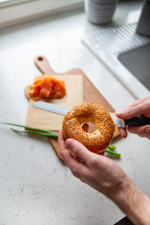 Preparing a breakfast. Male hands cutting a bagel with sesame with a knife. Breakfast concept with a...