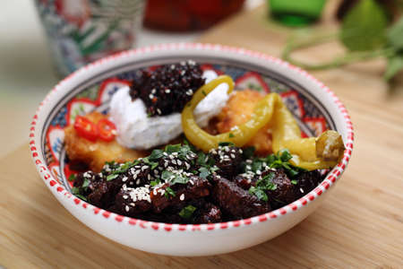 Vegan stew in a bowl served with rosti potato pancakes, sour cream, pickles, on a wood table, close-up, selective focus.の写真素材