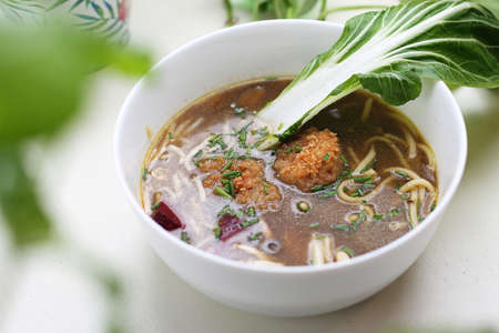 An oriental soup with bok choy, noodles and vegan meatballs in a bowl, on a table, a selective focus.の写真素材