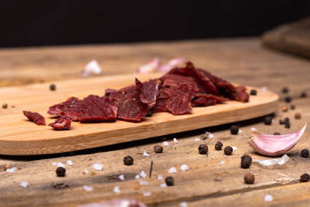 Rustic composition with seasonings, garlic and beef jerky, dried beef meat chips on wood cutting board, horizontal view.の写真素材
