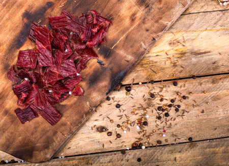 Beef jerky on wooden cutting board, top view. Dried beef meat chips and seasonings, composition on...
