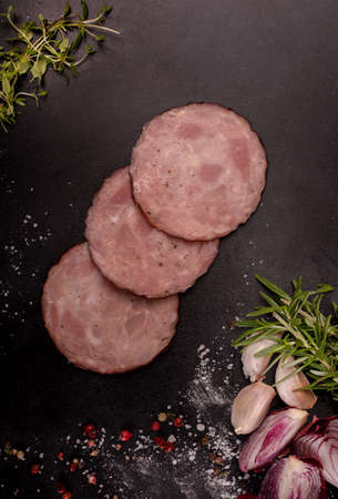 Sliced sausage, cold cuts, fresh herbs, garlic and spices on a black stone background, blackboard.の写真素材