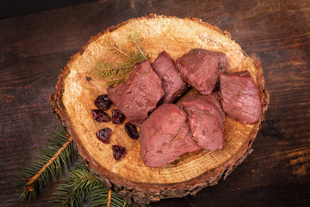 Raw game meat, beef on chopping block, wood slice. Steaks, pieces of red meat on wood. High quality roe, deer meat.の写真素材