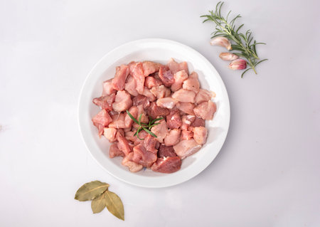 Diced meat on a white plate, isolated. Raw poultry, pork meat in cubes and seasonings, on white background.の写真素材