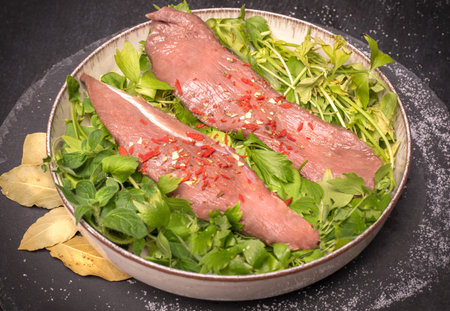 Raw pork tenderloin, sirloin and fresh herbs on a plate, on black background. Cooking concept with raw meat.の写真素材
