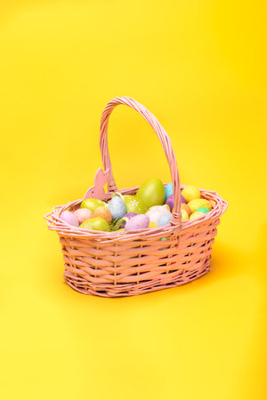 Easter basket full of colorful Easter eggs, on a yellow background. Easter holiday concept, photo with a copy space.の写真素材