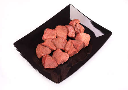 Raw game meat, beef on black plate, isolated. Diced red meat, on a white background. High quality roe, deer meat.の写真素材