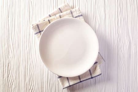 Empty plate on checkered tablecloth on white wooden tableの写真素材