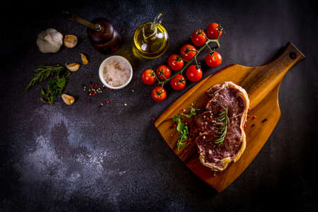 Beef steak on a wooden chopping board with vegetables and spices on black backgroundの写真素材