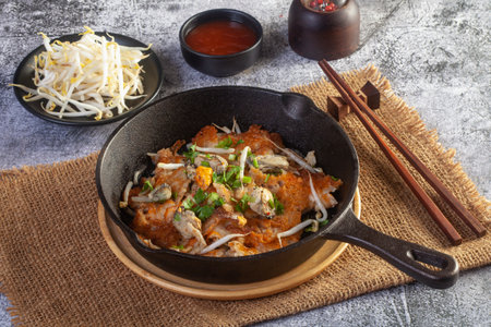 Hot pan of crispy fried oyster omelette served with bean sprout and spicy sauce.の写真素材