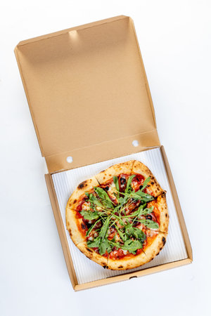 Home made pizza topped with black forest ham, tomatoes, spices, black olives, in a box isolated on a white backgroundの写真素材