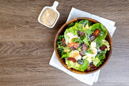 Salad with Fried Bacon, romaine lettuce, tomatoes and sauce known as Caesar salad served on plate, wooden table backgroundの写真素材