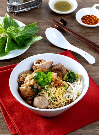 Stewed beef noodles, a Thai street food, and vegetables in a bowl on a wooden table.の写真素材