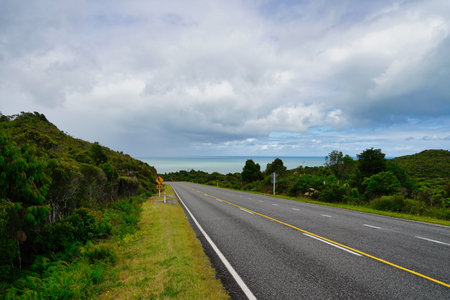 New Zealand road, roadsign, landscape with ocean, green trees and a sky with clouds
