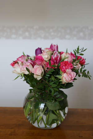 bouquets of roses, cloves and tulips in vase on table with white and gray backgroundの写真素材