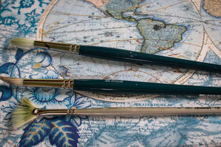 Fanned paint brushes on a vintage map, close-up, teal and silver coloured stems with dirty bristles.の写真素材