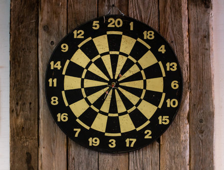 Black and yellow dartboard against a rustic wood backdrop - darts are arranged in a bullseye in a...