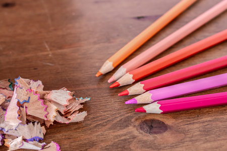 Pencil crayon shavings spilling out of a blue pencil sharpener with no lid on to a hardwood desk,...