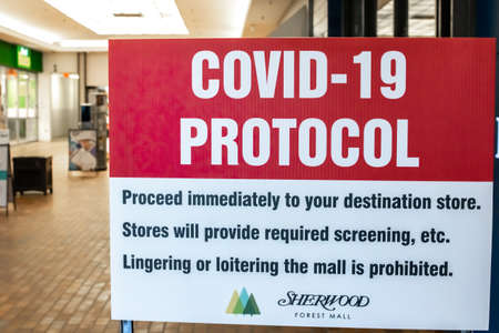 London, Ontario, Canada - February 28 2021: A red and white COVID-19 protocol sign at the entrance of Sherwood Forest Mall. Proceed to destination store immediately. Loitering or lingering prohibited.のeditorial素材