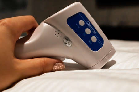 Bridgetown, Barbados - March 24 2021: Closeup of a woman's manicured hand holding a digital forehead temperature scanner - thermometer - side view, no reading visible. Quarantine instrument.のeditorial素材