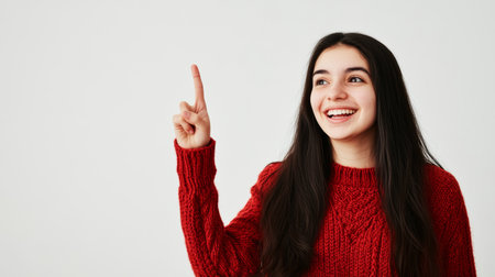 a smiling woman in a red sweater points upwards, set against a simple studio backdrop. she looks cheerful.の素材