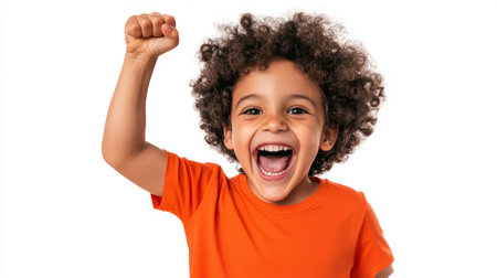 a young child with curly hair is raising his fist and smiling widely with an orange shirt on a plain settingの素材