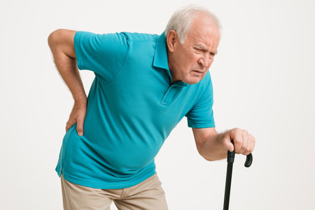 a senior man in a turquoise shirt is holding a walking stick and experiencing physical discomfort or pain.の素材