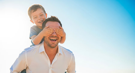 A cheerful father and son share a joyful moment, with the son covering his father's eyes, creating a heartwarming scene.の素材