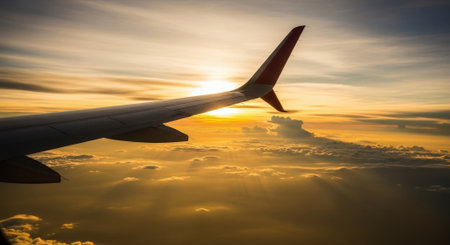 View from an airplane window showcasing the aircrafts wing against a stunning backdrop of a golden sunset and fluffy clouds, creating a serene and picturesque travel scene.の素材
