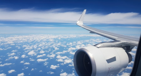 View from an airplane window showing the wing and engine above a sea of clouds and a clear blue sky, capturing the essence of air travel.の素材